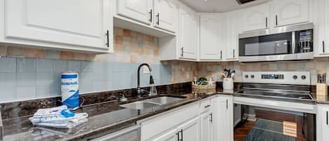 Cocina moderna con gabinetes blancos, encimera negra, lavavajillas Whirlpool, microondas y horno.