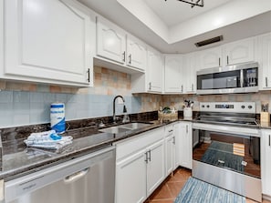 Cocina moderna con gabinetes blancos, encimera negra, lavavajillas Whirlpool, microondas y horno.