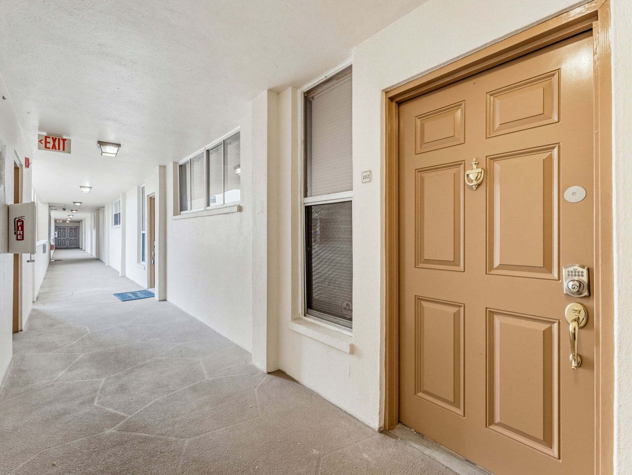 A hallway with a fire alarm, exit sign, and a door with a keypad lock.