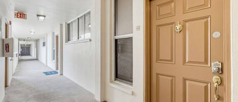 A hallway with a fire alarm, exit sign, and a door with a keypad lock.
