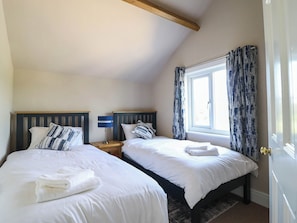 Une chambre avec deux lits, une fenêtre avec des rideaux, une table de chevet avec une lampe et une porte.