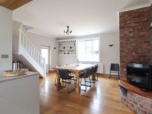 A dining area with a wooden table and chairs, a chandelier, and a brick fireplace. - Pwll Glas (Caersws)