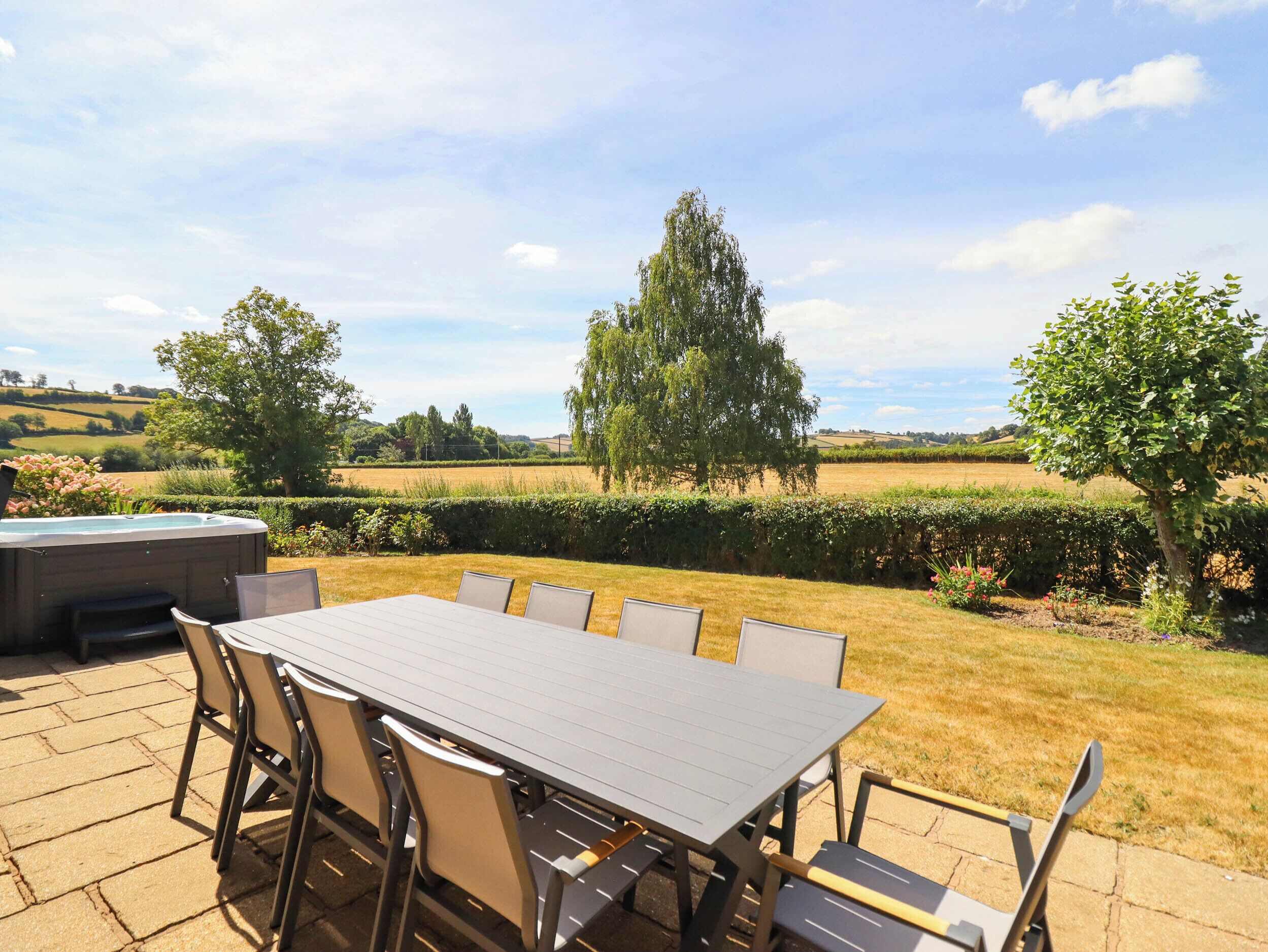 Une terrasse extérieure avec une table et des chaises, un jacuzzi et une vue sur un paysage rural.