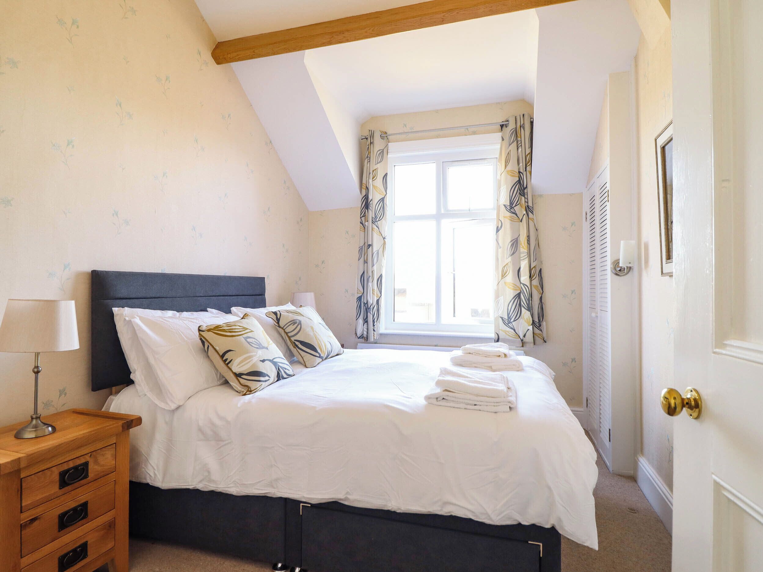 A bedroom with a bed, a nightstand, a window with curtains, and a door.