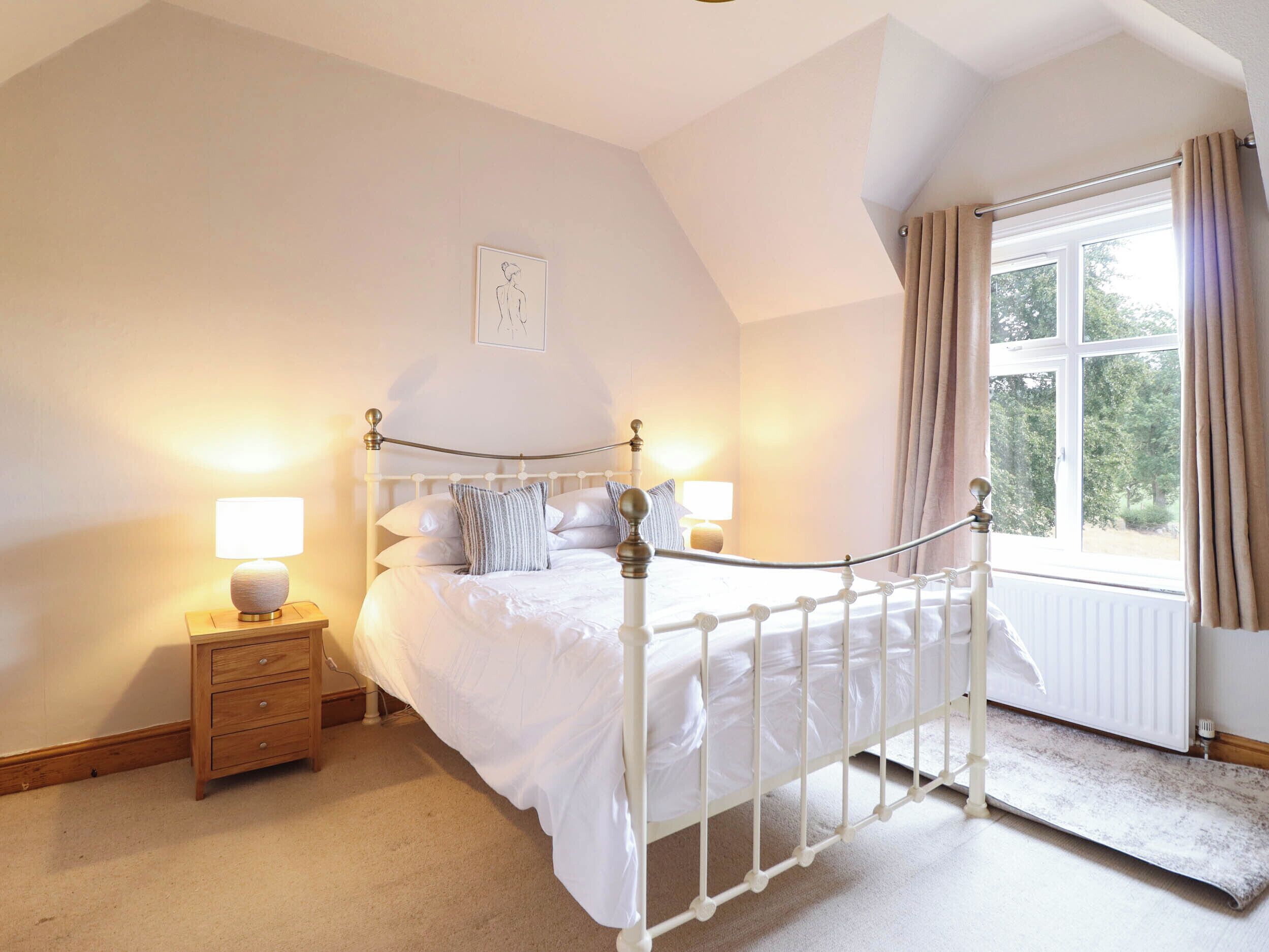 A bedroom with a white four-poster bed, two bedside tables with lamps, a window with curtains, and a radiator.