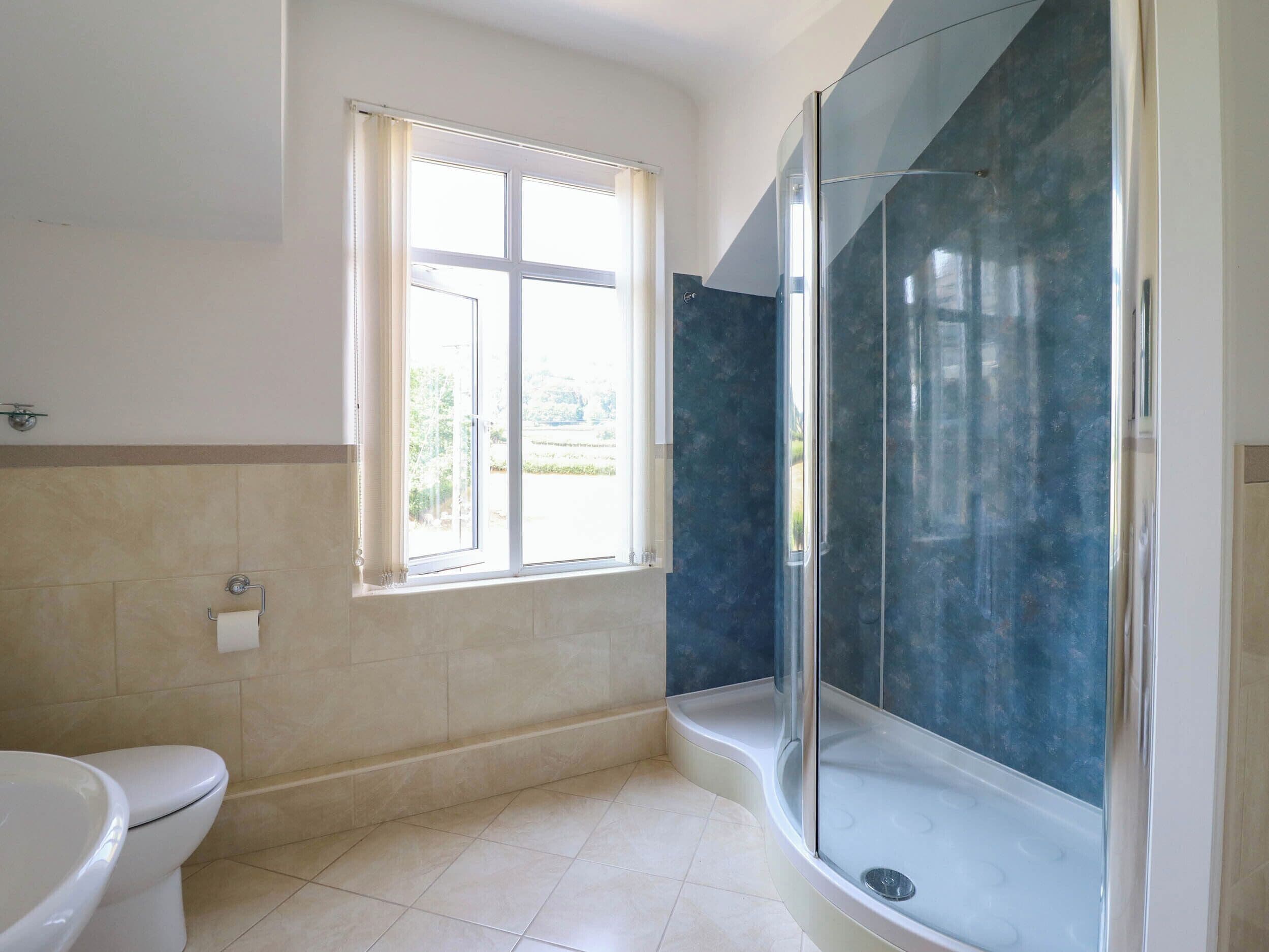 A bathroom with a toilet, a window, and a glass-enclosed shower area.