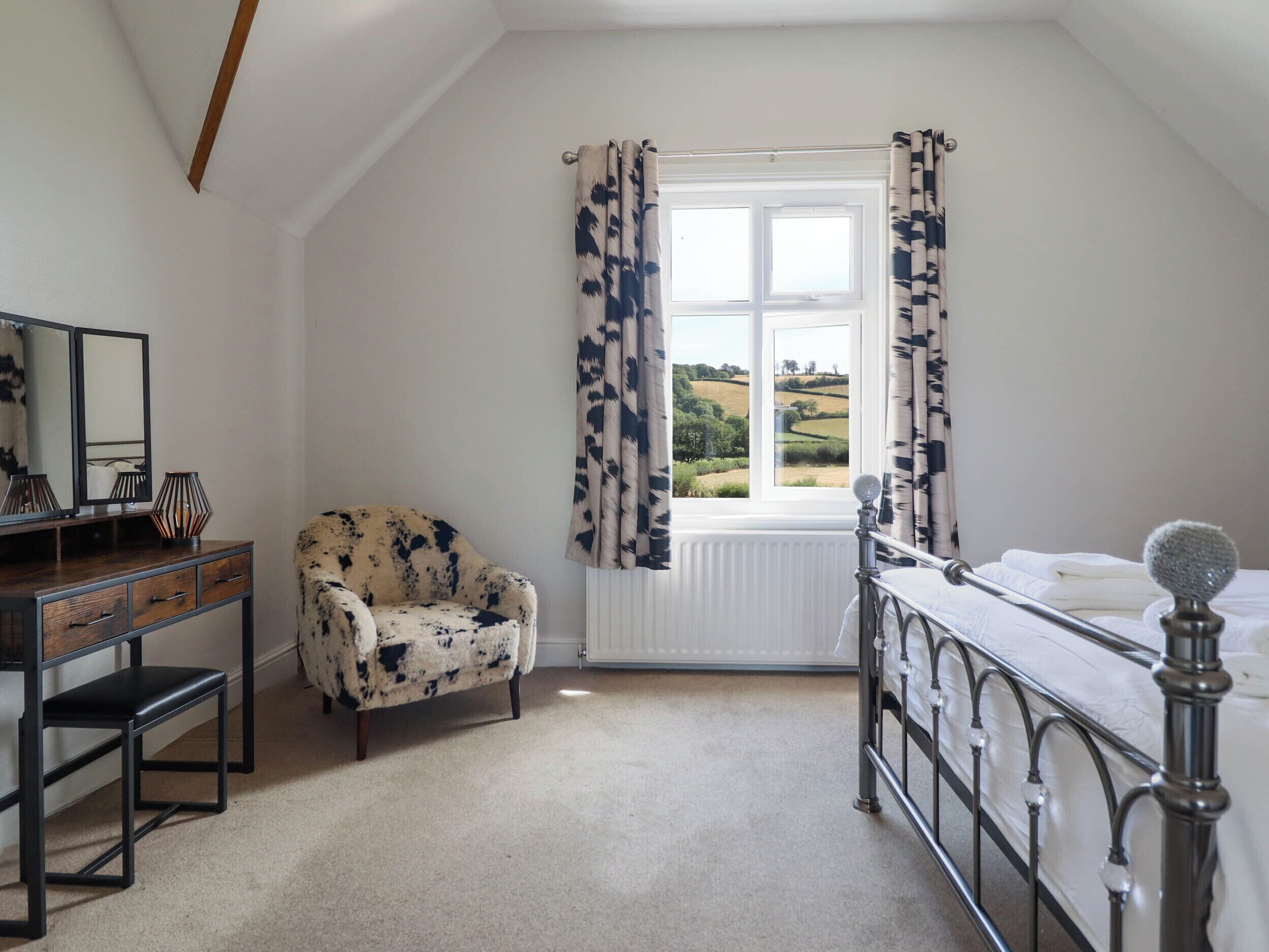 A bedroom with a bed, a chair, a dresser, a mirror, and a window with curtains.