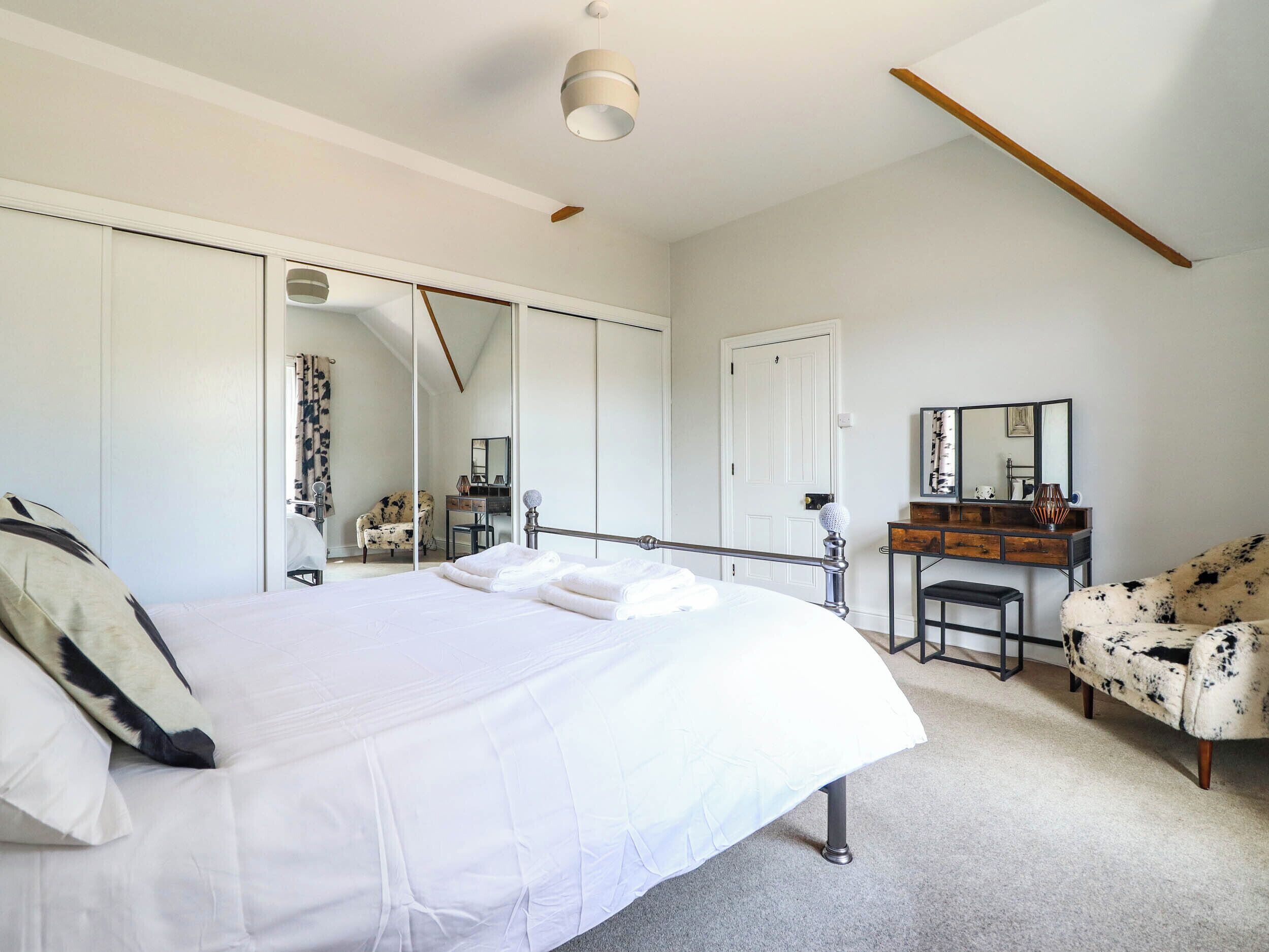 A bedroom with a bed, a chair, a dresser, a mirror, and a wardrobe.