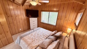 A wooden-paneled bedroom with a bed, a ceiling fan, a TV, and a window. - Serenity Now by Innsbrook Vacations! (Wright City)