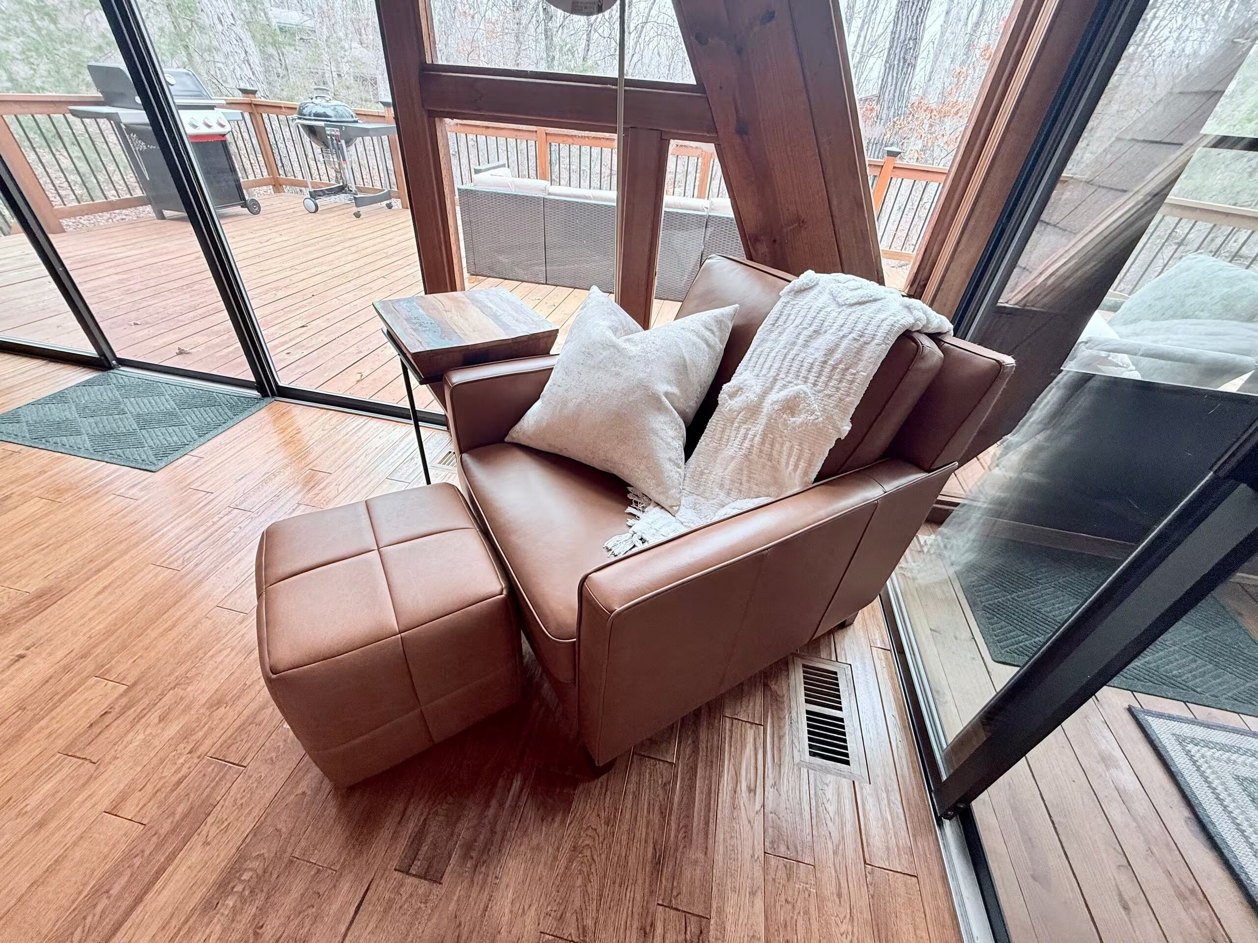 Et værelse med en brun lædersofa, et lille sofabord og udsigt til en udendørs terrasse med grill.