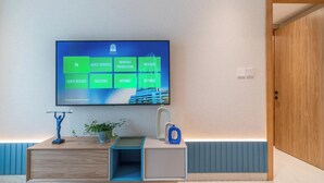 Ein Hotelzimmer mit einem großen Flachbildfernseher an der Wand, einer Holztür und einem kleinen Tisch mit Pflanze und blauer Vase.