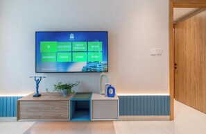 Ein Hotelzimmer mit einem großen Flachbildfernseher an der Wand, einer Holztür und einem kleinen Tisch mit Pflanze und blauer Vase.