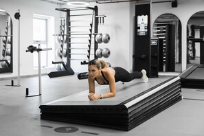 Ein Fitnessraum mit Trainingsgeräten, einer Person im Plank und einer Spiegelwand.