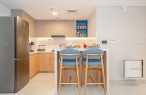 Eine moderne Küche mit einem Edelstahl-Kühlschrank, Holzschränken und einer Sitzgelegenheit mit blauem Barhocker.