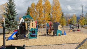 Un parque infantil con diversas estructuras de juego, rodeado de árboles con hojas otoñales.