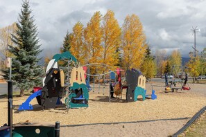 Ein Spielplatz mit verschiedenen Spielgeräten, umgeben von Bäumen mit Herbstlaub.