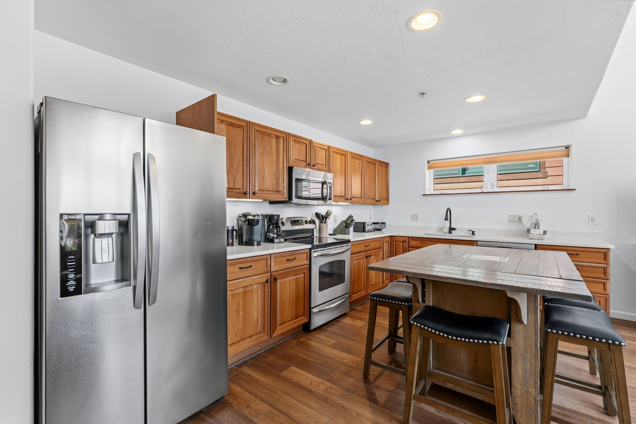 A modern kitchen with stainless steel appliances, wooden cabinets, and a bar area with stools.