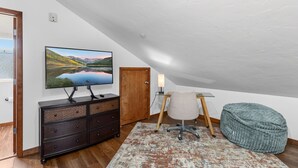 Una habitación con una televisión sobre una cómoda, un escritorio con lámpara, una silla y un sillón de saco.