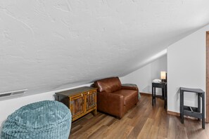 A loft-style room with a sloped ceiling, a brown leather sofa, a wooden cabinet, a blue bean bag, and a small table with a lamp. - Frisco Mountain Condo | Fireplace, Garage and Great Location (Frisco)