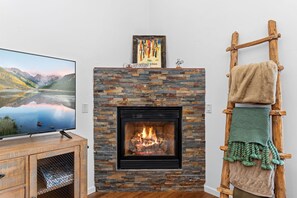 A fireplace with a stone facade, a television on a wooden stand, and a wooden ladder with towels. - Frisco Mountain Condo | Fireplace, Garage and Great Location (Frisco)