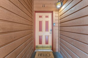A wooden door with a red and beige color scheme, a doormat with 'HELLO' written on it, and a wall-mounted light fixture. - Frisco Mountain Condo | Fireplace, Garage and Great Location (Frisco)