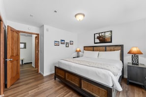 A bedroom with a wooden bed, two bedside lamps, a headboard with a framed picture, and a door leading to another room. - Frisco Mountain Condo | Fireplace, Garage and Great Location (Frisco)