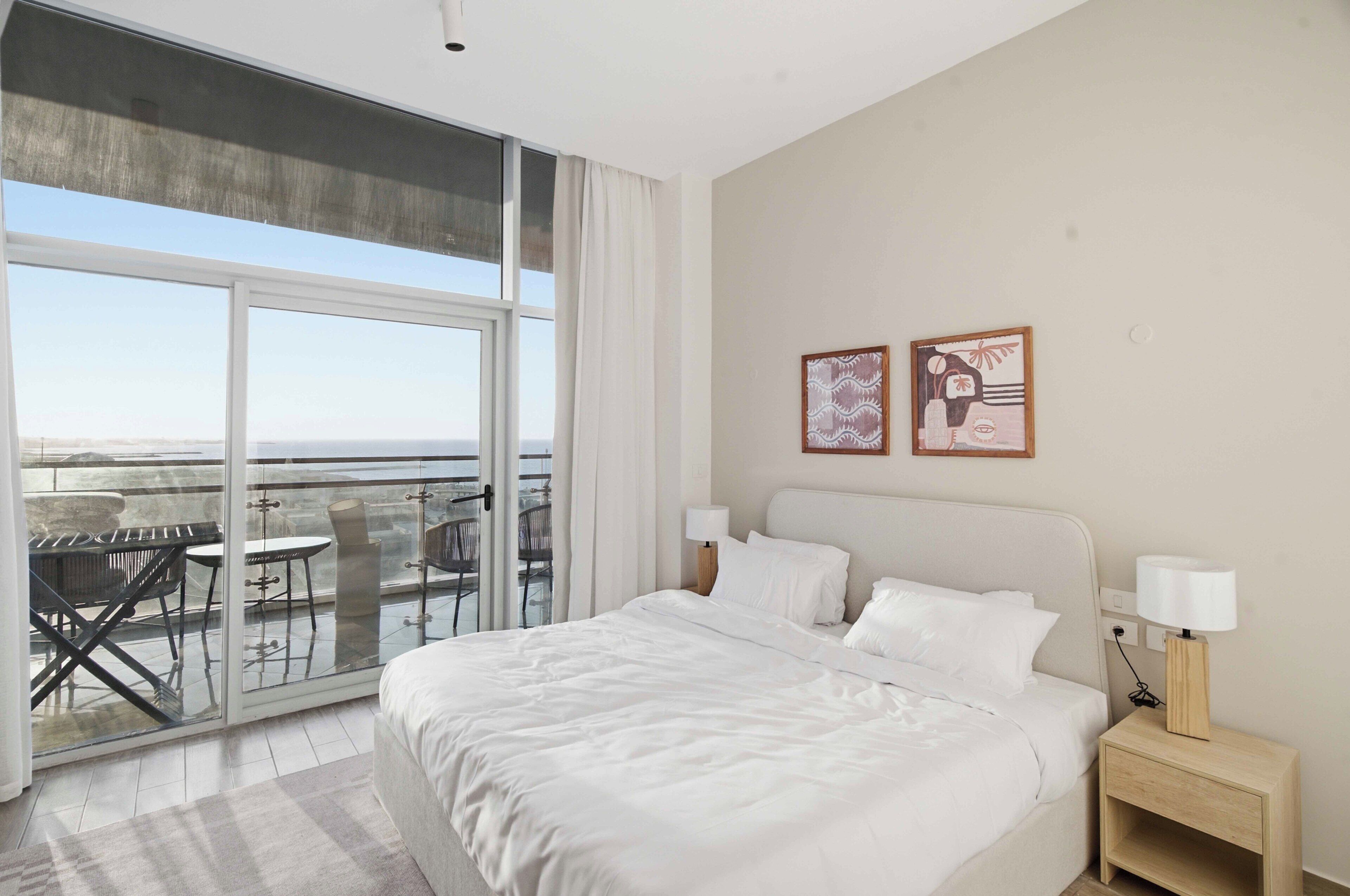 Ein Hotelzimmer mit einem großen Bett, zwei Nachttischlampen, einem Nachttisch, Blick auf den Balkon und zwei Wandbildern.