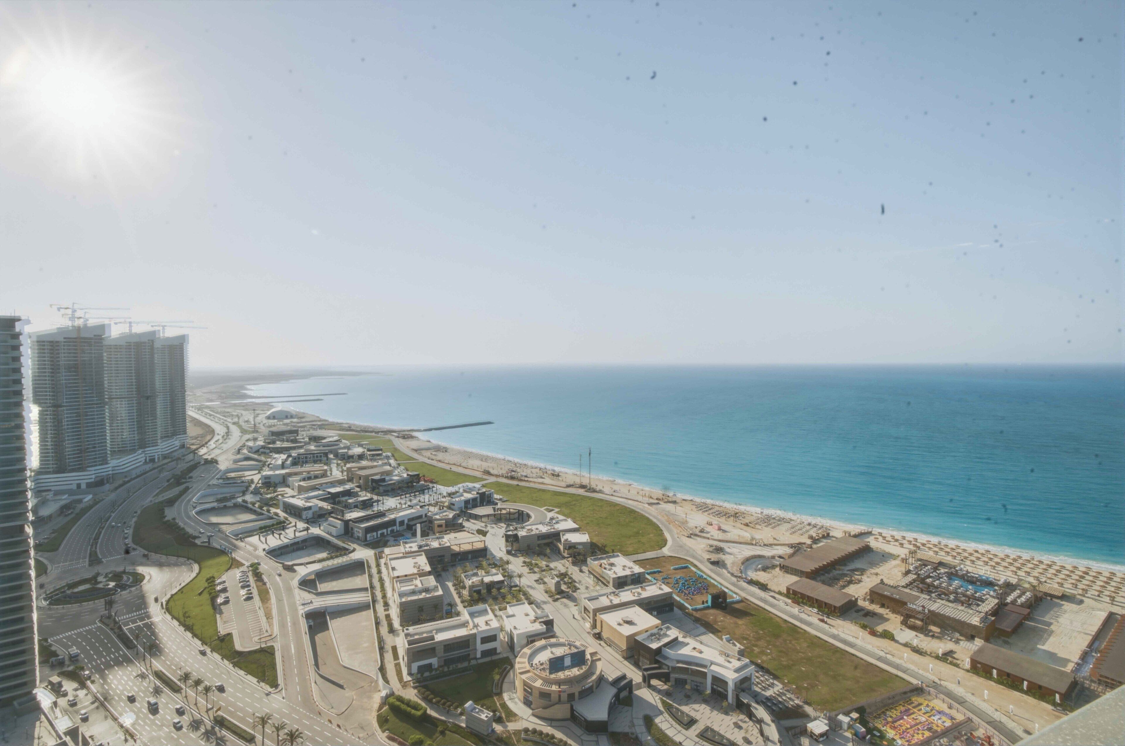 A coastal cityscape with high-rise buildings, a beach, and a marina.