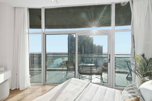 A modern bedroom with a large glass balcony, a bed, and a view of a cityscape.