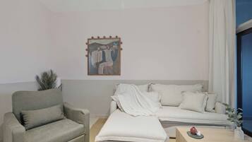 A modern living room with a grey armchair, a white sofa, a small wooden table, and a painting on the wall.