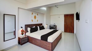 A modern bedroom with a large bed, a bedside table with a vase of flowers, a mirror, and a ceiling light. - Super OYO Collection O Prayag Junction (Prayagraj)