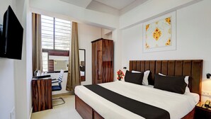 A hotel room with a bed, a desk, a wardrobe, a television, and a window with curtains. - Super OYO Collection O Prayag Junction (Prayagraj)