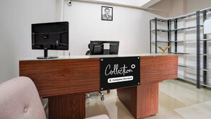 A reception desk with a 'Collection' sign, a framed portrait on the wall, and a metal shelving unit in the background. - Super OYO Collection O Prayag Junction (Prayagraj)