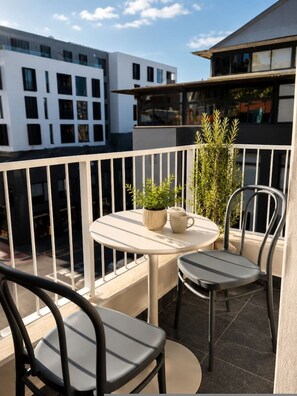 A balcony with a round table, two chairs, a potted plant, and a railing. - Balcony Suite The Valour in De Waterkant (Cape Town)