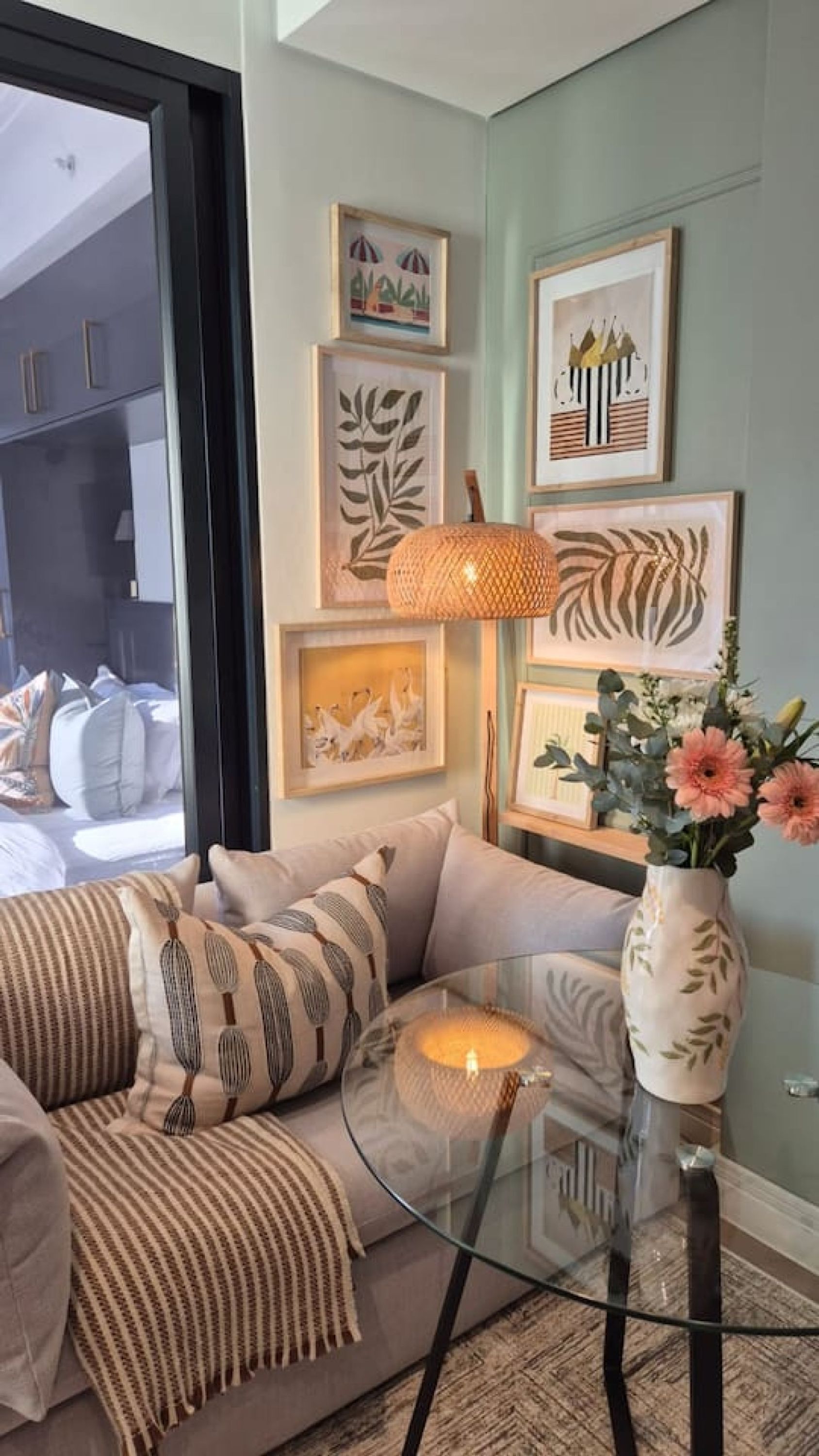 A living room with a sofa, a glass coffee table, and a vase with flowers.
