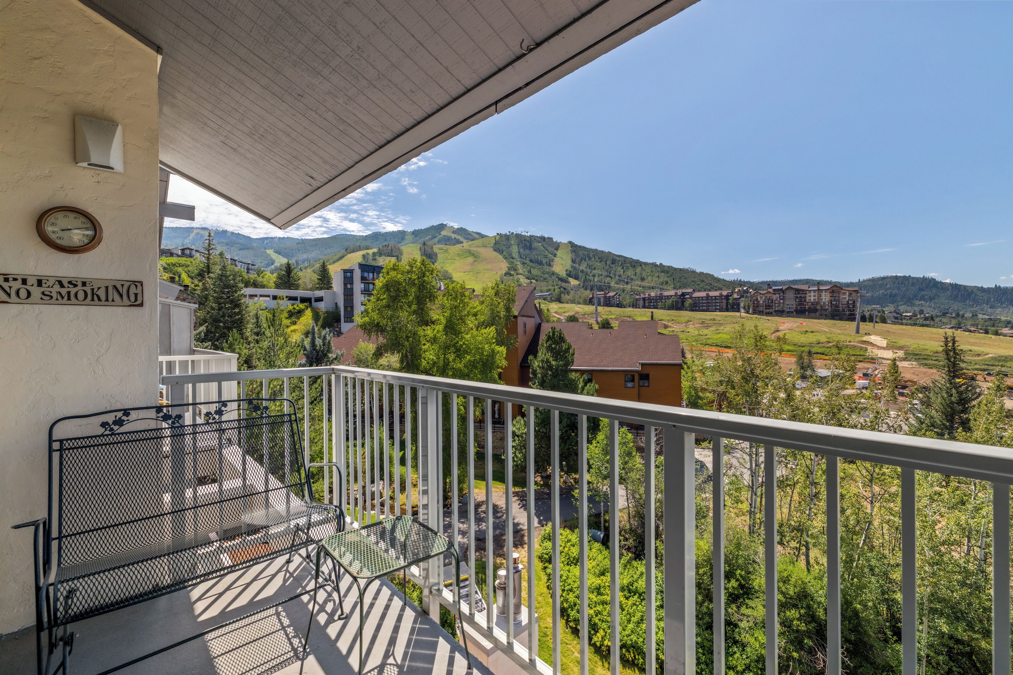 A balcony with a metal chair and a 'NO SMOKING' sign, overlooking a mountainous landscape with buildings.