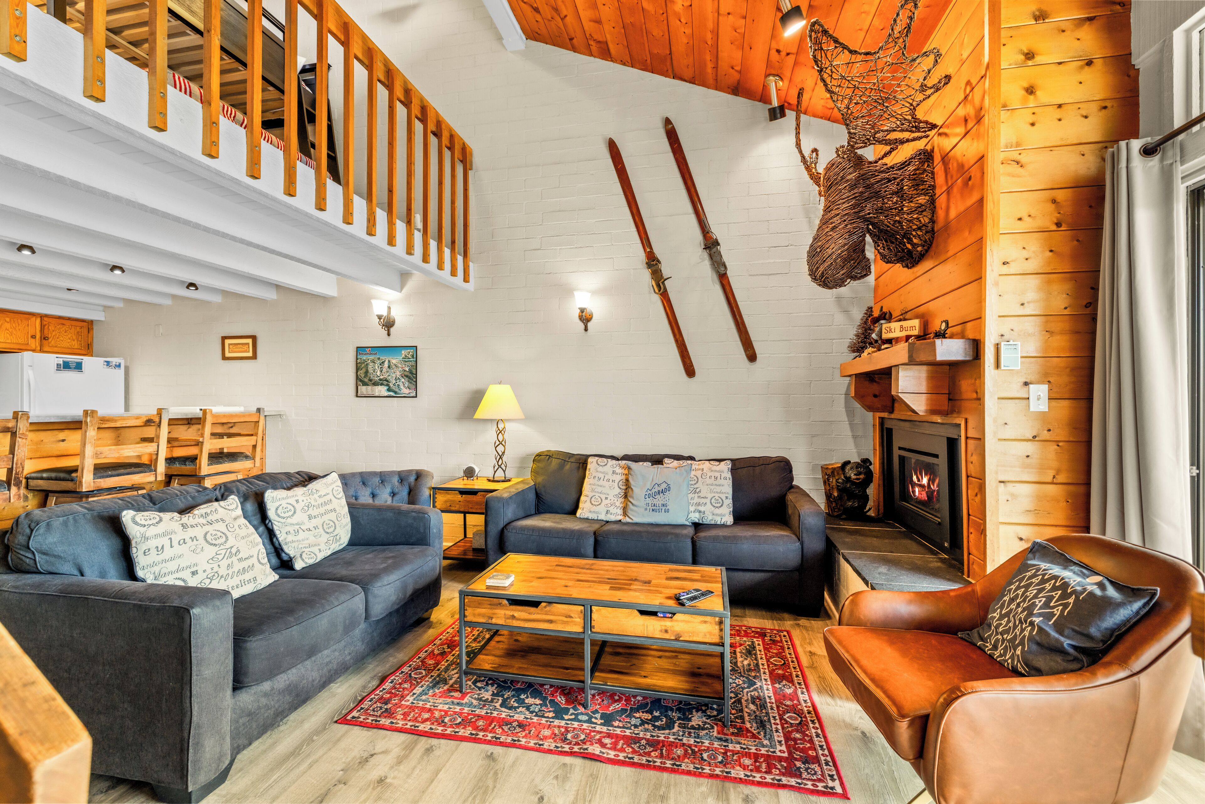 Ein gemütliches Wohnzimmer mit Kamin, Holzbalkendecke und einer an der Wand befestigten Skiaufbewahrung.
