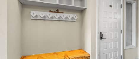 Een gang met een houten bankje, een witte deur en een kapstok aan de muur.
