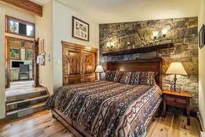 Une chambre avec un mur en pierre, un lit en bois et un escalier menant à un espace extérieur.