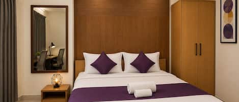 Habitación de hotel con una cama grande, un armario de madera, un escritorio con lámpara y un espejo.