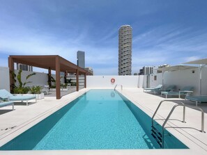 A rooftop swimming pool with a clear view of a tall, cylindrical building in the background. - StayShort - Contemporary Studio Sleeps 2 in JVC (JVC)