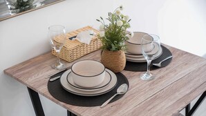 A dining table set with plates, bowls, cutlery, and glasses, accompanied by a woven basket and a potted plant. - StayShort - Contemporary Studio Sleeps 2 in JVC (JVC)