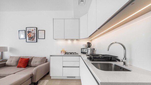 A modern kitchen with white cabinetry, a stainless steel sink, and a built-in stove. - StayShort - Contemporary Studio Sleeps 2 in JVC (JVC)