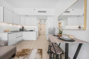 Una cuina moderna amb armaris blancs, una illa central i una zona de menjador amb taula i cadires de fusta.