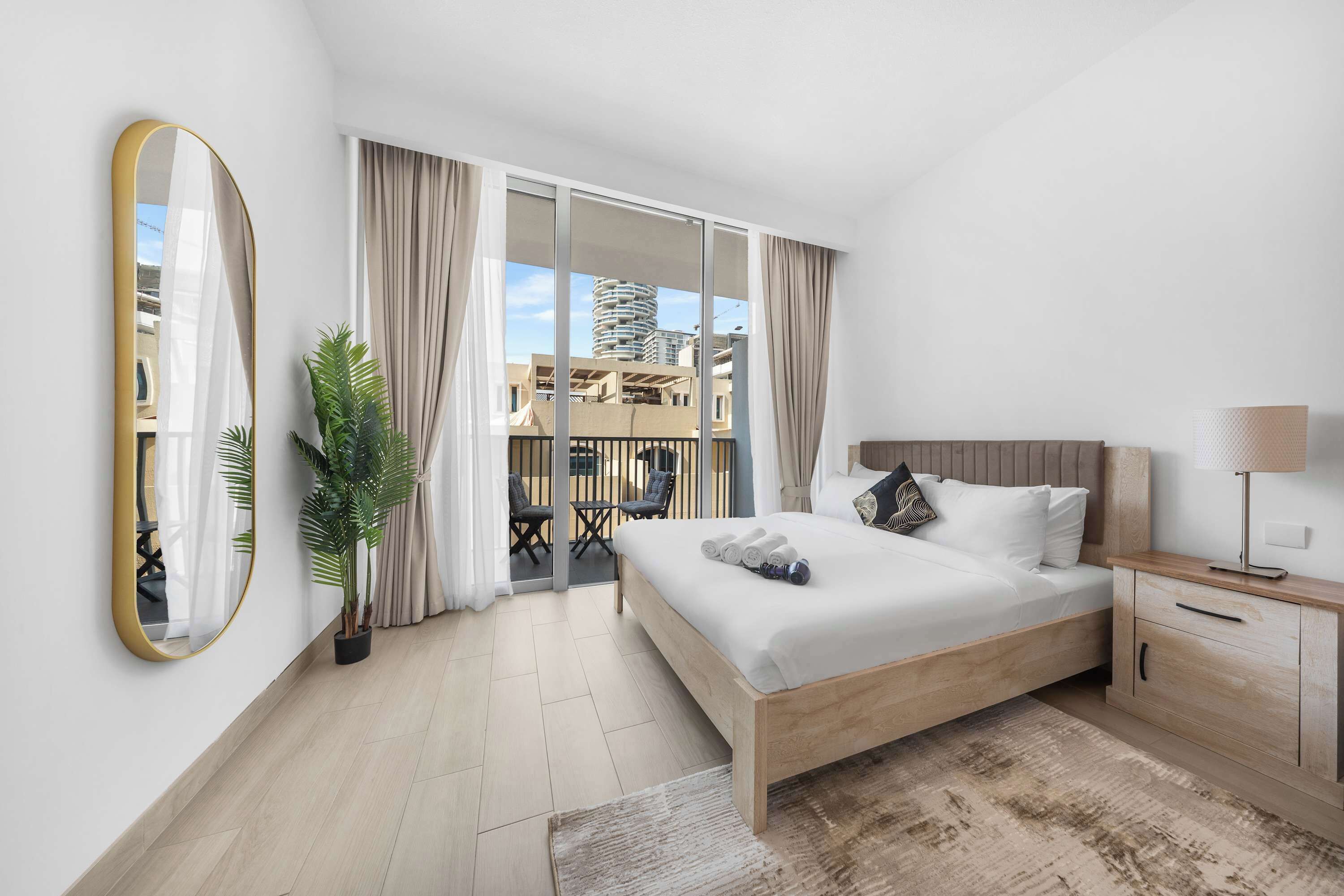 Een hotelkamer met een bed, nachtkastje, lamp, kamerplant en uitzicht op de stad.