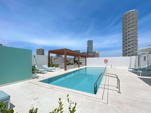 Ein Pool auf dem Dach mit Liegestühlen und einer Pergola, umgeben von Stadtgebäuden.