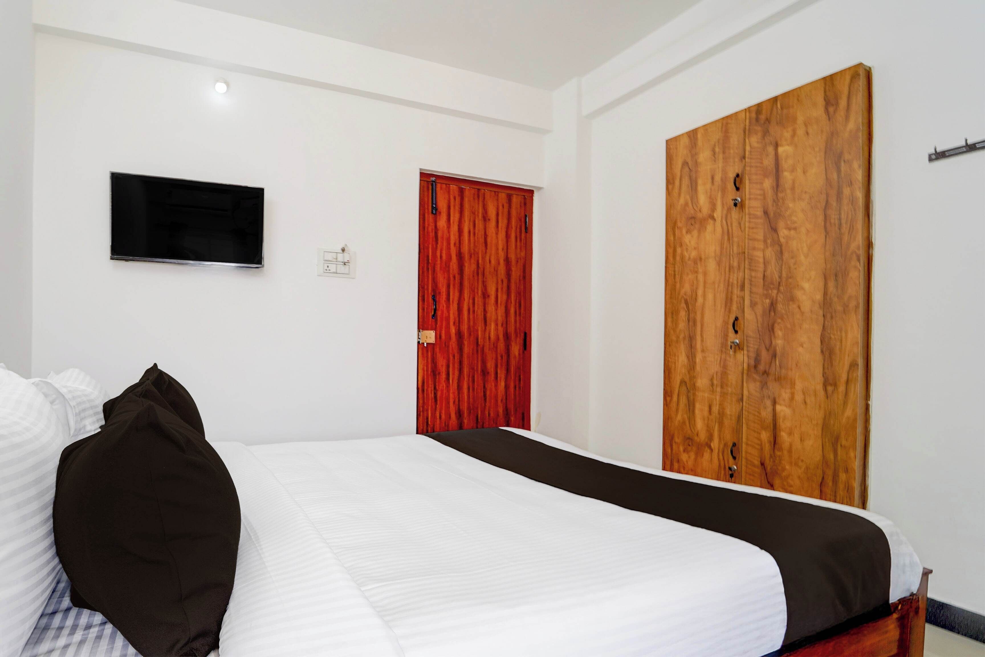 Un dormitorio con una cama, un televisor montado en la pared y dos puertas.
