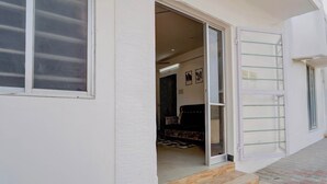 Entrada de un edificio con puerta corredera de vidrio, unos escalones de madera y un pequeño espacio exterior con un tapete estampado.