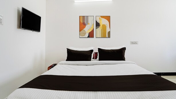 Habitación de hotel con cama, televisión de pantalla plana en la pared y dos cuadros abstractos sobre la cama.
