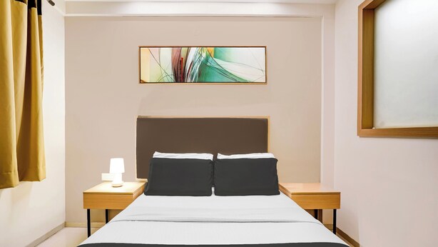 A hotel room with a bed, two bedside tables, a lamp, a painting on the wall, and a window with curtains. - Collection O Metro Park Opp Kalasipalya (Bangalore)